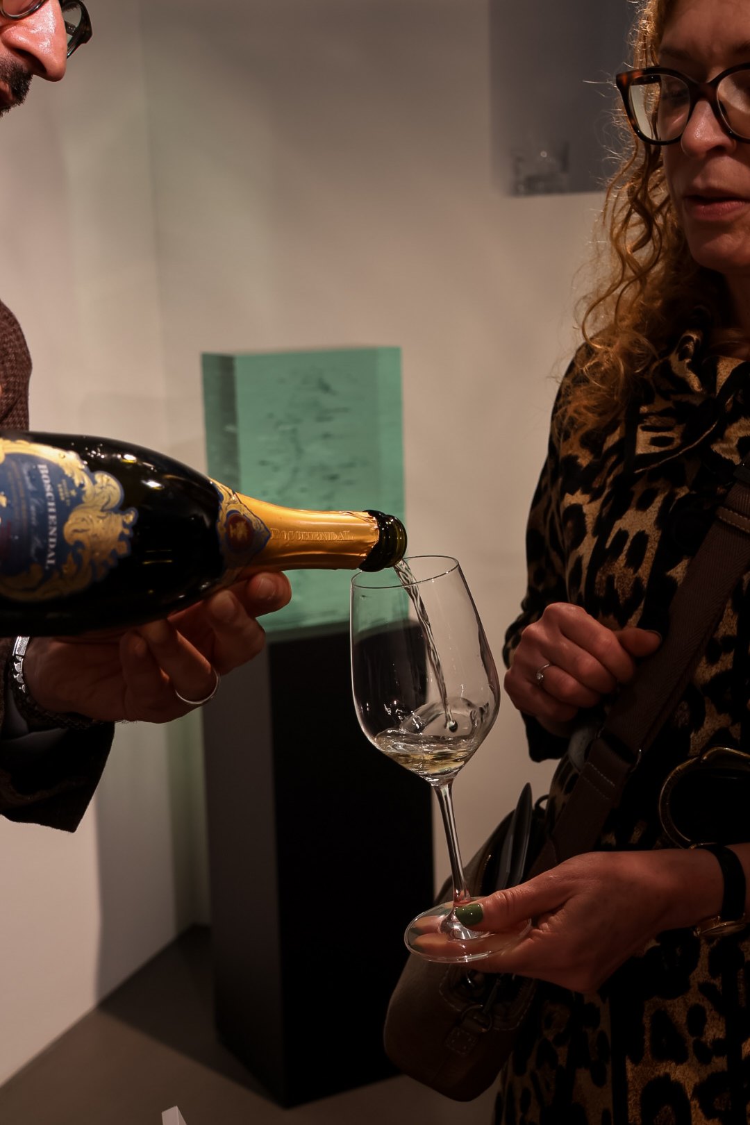 Schaumwein wird bei einer Vernissage in ein Glas geschenkt