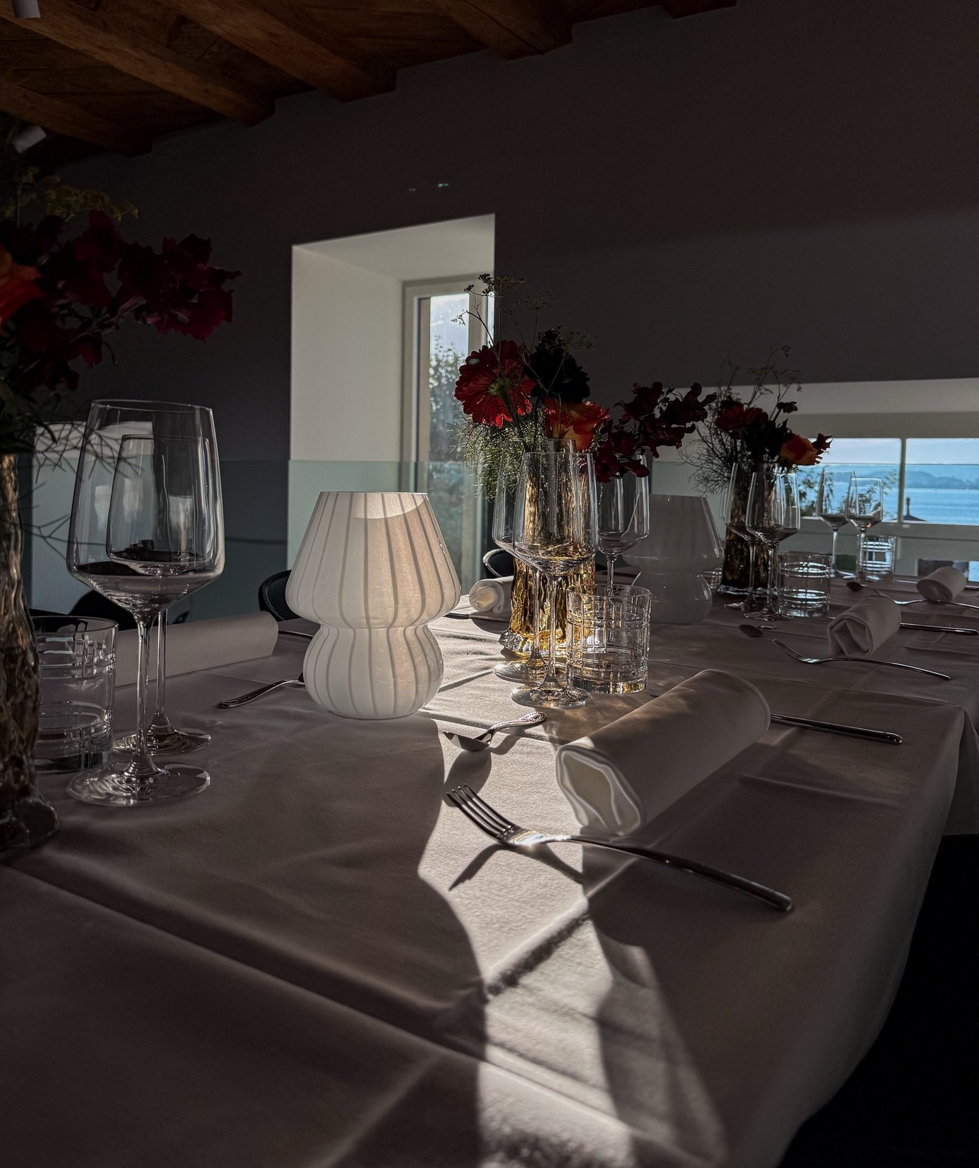 Gedeckte Tafel mit Glaslampe und Blumen, im Fenster der See